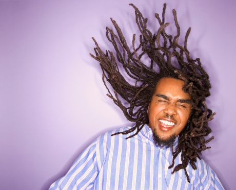African-American young adult man on purple background with his dreadlocks in motion.
