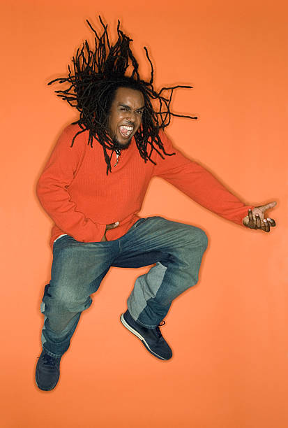 Man jumping and playing air guitar. African-American young adult man on orange background jumping while playing air guitar. air guitar stock pictures, royalty-free photos & images