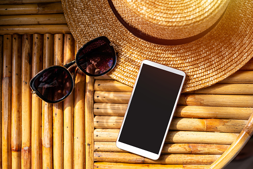 Empty screen smart phone with travel accessories on wooden table, Summer vacation concept