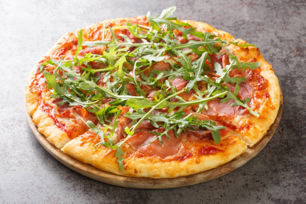 istock Hot pizza with prosciutto and arugula close-up on a wooden board. Horizontal 1458508904