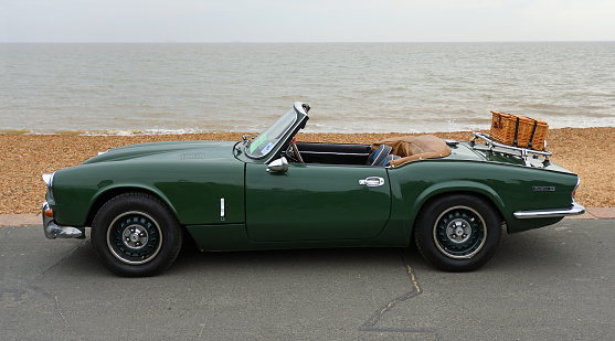 Felixstowe, Suffolk, England - May 01, 2022: Classic Green Spitfire Mk 4  motor  car with picnic basket on boot parked on Seafront Promenade beach and sea in background.