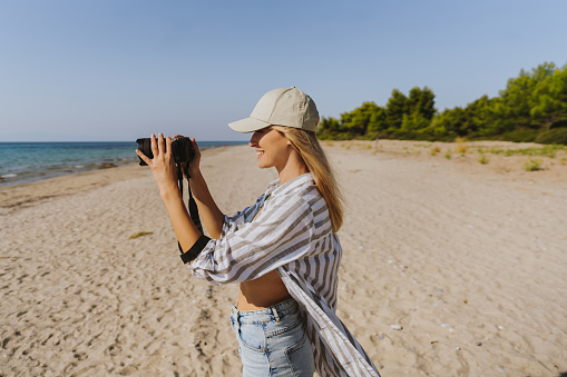 Photo of a smiling young woman, spending time on the local beach and taking photos to remember that perfect summer afternoon