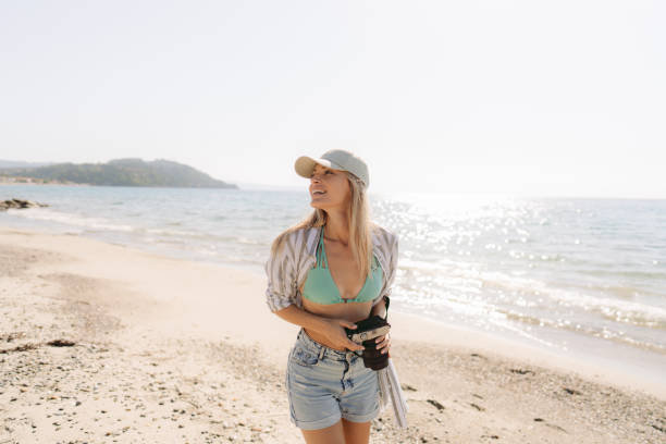 Photo of a smiling young woman, spending time on the local beach and taking photos to remember that perfect summer afternoon