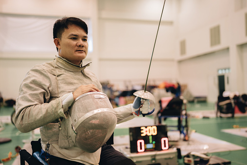Portrait of a male fencer that takes off his fencing mask in gym.