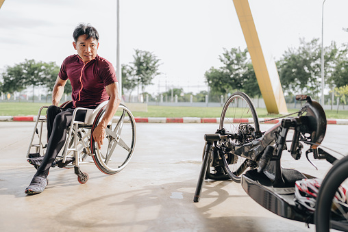 A para athlete men prepares to train on a stadium track with his racing wheelchair. He is sitting in his wheelchair and getting his gear together.