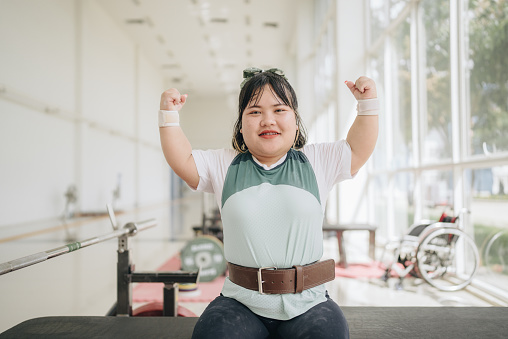Young adult physically disabled using a wheelchair are in an indoor gym lifting hand weights.