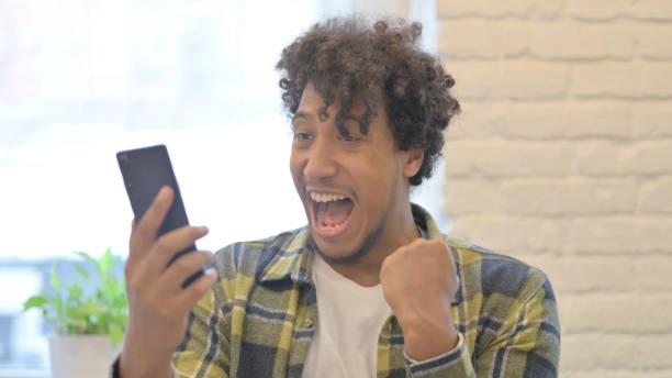 istock Excited African Man Celebrating Win on Smartphone 1458512163