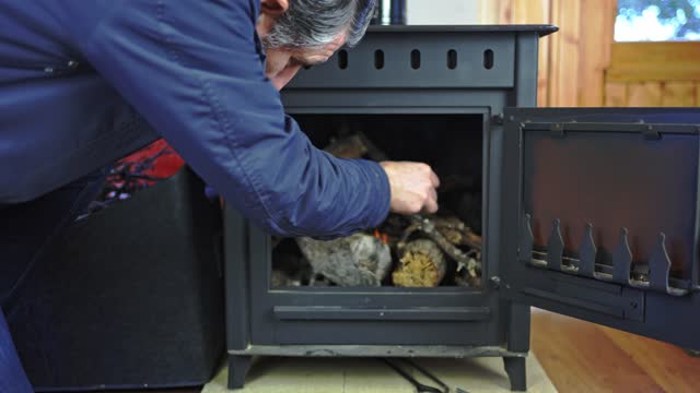 Man lighting the fire inside a rustic cast iron stove to heat the house.