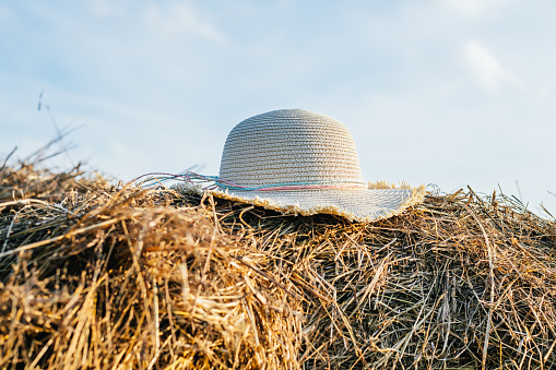 Wicker female panama hat lying at top of haystack. Beautiful clear blue sky. Pile of dry grass. Countryside lifestyle.