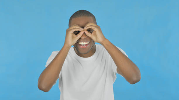 istock Excited African Man Searching with Handmade Binocular on Blue Background 1458515200