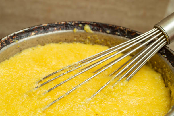 Boiling corn flour in a cast iron pot, making mamaliga, traditional romanian food, Boiling corn flour in a cast iron pot, making mamaliga, traditional romanian food, and mixing with a stainless steel whisk, soft focus close up mamaliga stock pictures, royalty-free photos & images