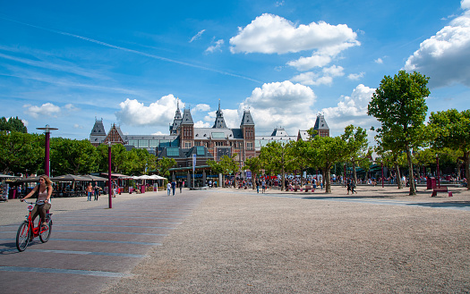 People walk and cycle through a park near the Rijksmuseum. It's a beautiful sunny day in the city of Amsterdam during the summer