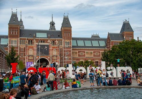A crowd of people beside the I am Amsterdam sign in front of the Rijksmuseum. It's a cloudy summer day in the city of Amsterdam