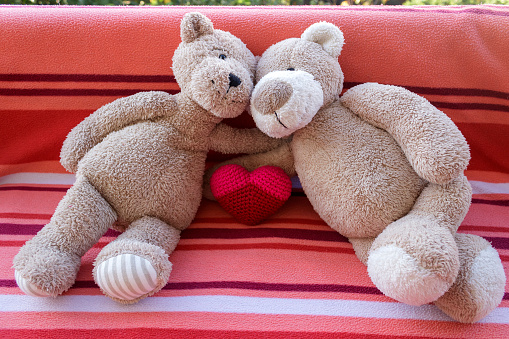 Teddy bear couple lying on sofa with red knitted heart