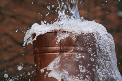 Water pouring into a copper pail. Focus is on pail.