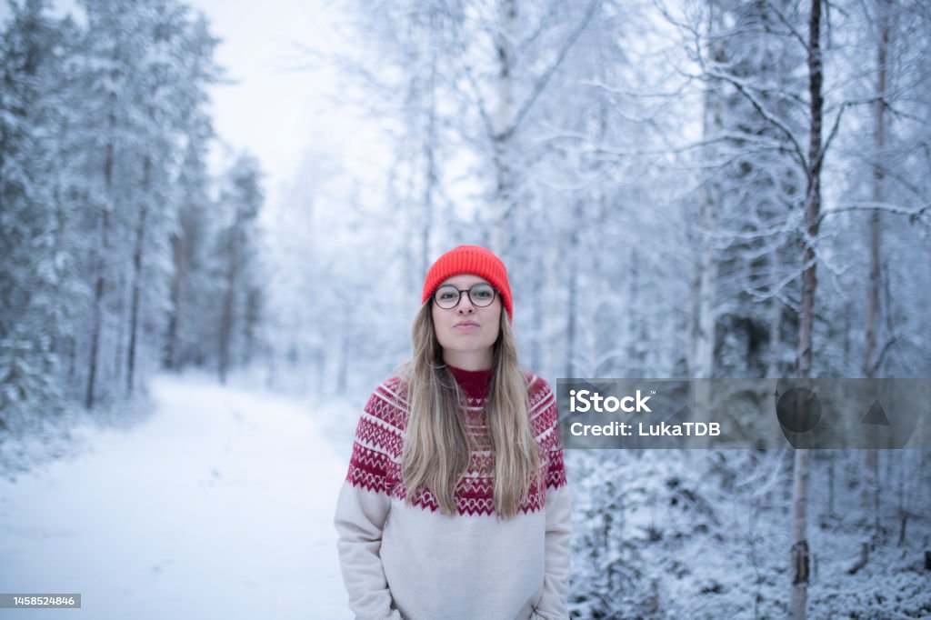 Portrait of a woman walking on a winter day surrounded by a pine forest Waist up view of a lovely woman with a Nordic style hat enjoying a winter day outdoors Finland Stock Photo