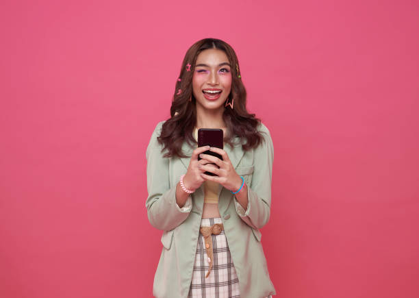 istock Happy Asian woman using mobile phone isolated on pink background. 1458526390