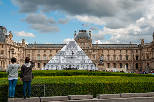 Tours take pictures in the courtyard of the Louvre Museum with beautiful Hedges and the glass pyramid. Taken during the summer in the city of Paris