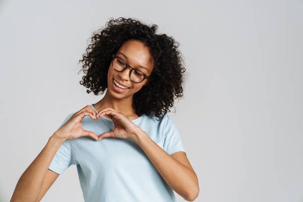 Femme noire bouclée portant des lunettes souriant tout en faisant un geste cardiaque - Photo