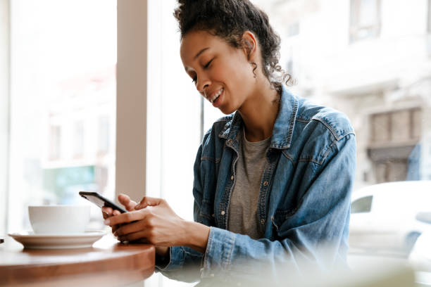istock Black young woman using cellphone while drinking coffee in cafe 1458532458