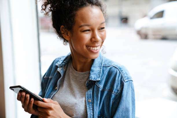 istock Black young woman using cellphone while standing by window in cafe 1458532661