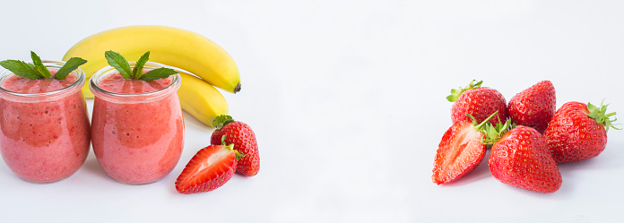 Smoothie with strawberry and banana in the glass jar and ripe strawberry on the white background. Copy space. Banner.