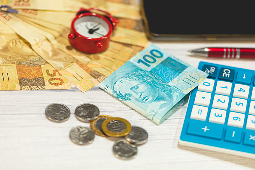Brazilian Real banknotes and coins on a wooden table. A calculator in the composition. Brazilian economy and finance.