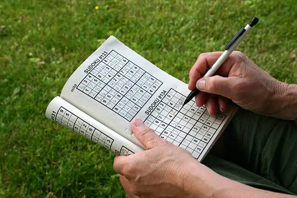 Woman doing a Sudoku Puzzle with a pencil in her hand.