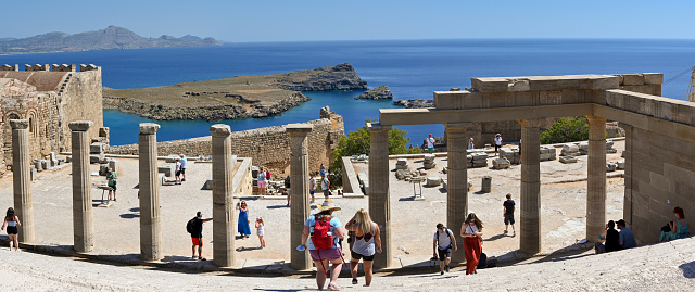 Lindos, Rhodes, Greece - May 2022: Panoramic view of tourists visiting the ancient ruins of the acropolis above the town