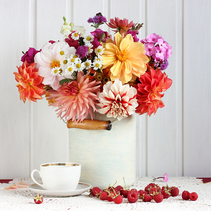 autumn still life, a bouquet of garden dahlias of different varieties in a can and raspberries, flowers and berries on the table.