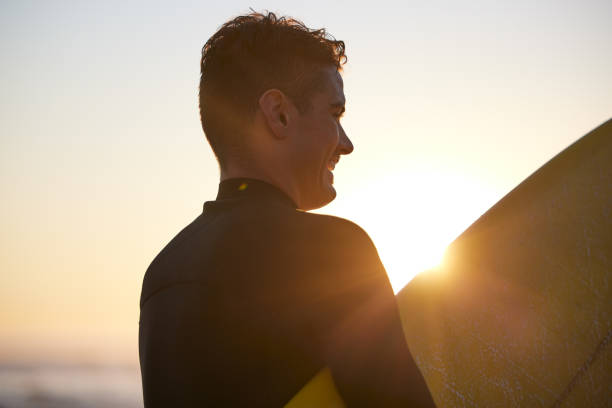 istock Fitness, sunset or man surfer with surfboard for exercise, workout or training wellness at the beach, ocean or sea with smile. Happy, freedom or lens flare male athlete for water sports motivation 1458555328