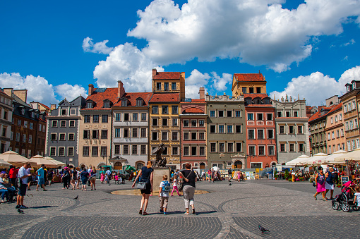 A wide shot of colorful residential buildings and shops in a courtyard full of people on a beautiful Summer's Day in the city of Warsaw