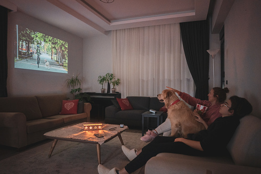 Happy family wit dog watching projector, TV, movies with popcorn in the evening at home