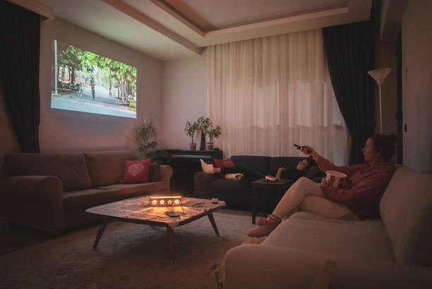 mulher assistindo cinema em casa projeção na sala de estar. - entertainment center watching tv television popcorn - fotografias e filmes do acervo