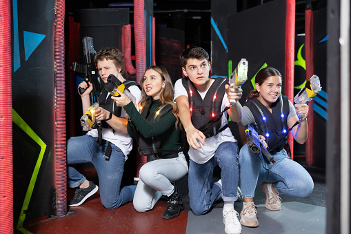 Positive girls and guys playing laser tag game opposite each other in modern dark room