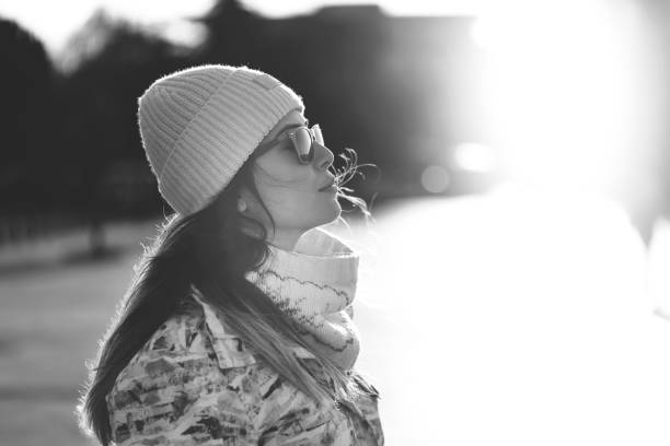 Beautiful lonely woman in a coat and scarf with her hair developing in the wind under a bridge on a cold gray day. The concept of loneliness. Black and white art photo. Soft selective focus.