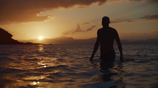 Spiritual man meditating in the sea. Watching beautiful orange setting sun. Praying and practicing wellness and mindfulness.