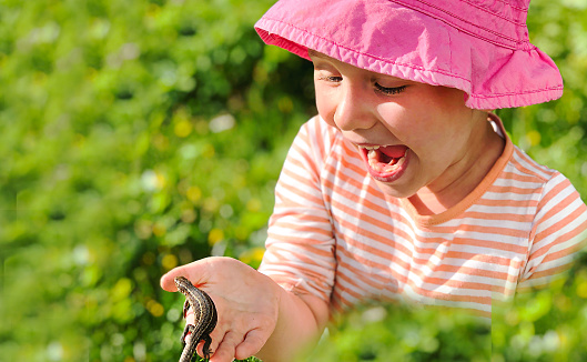Caucasian little girl exploring nature in a summer meadow looking at magnifying glass