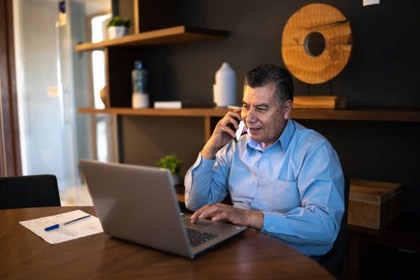 homem maduro usando laptop e tendo um telefonema no escritório - mexico only men senior men mature men - fotografias e filmes do acervo