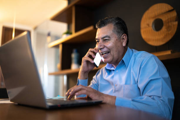 istock Mature man using laptop and having a phone call at the office 1458588594