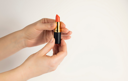 Female hands open a tube of red lipstick on a white background