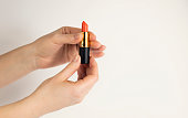 Female hands open a tube of red lipstick on a white background.