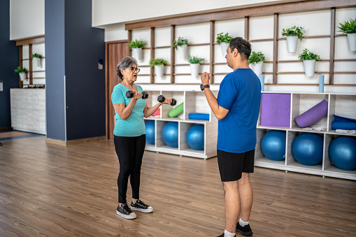 Fitness instructor assisting senior woman doing weightlifting at the gym