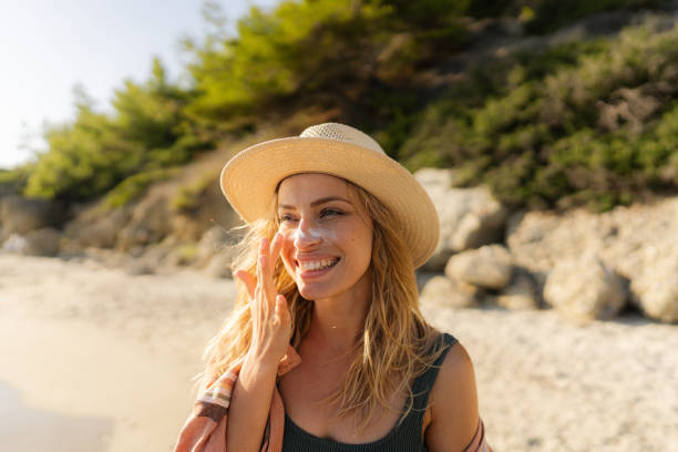 mujer joven aplicándose protector solar en la playa - crema de sol fotografías e imágenes de stock