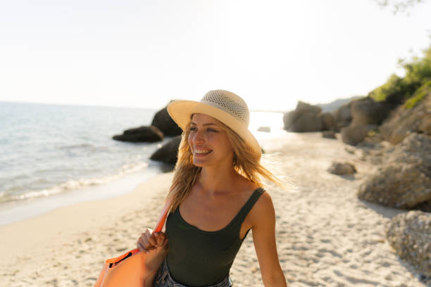 Smiling young woman at the beach Photo of a smiling young woman, wearing her hat and a beach bag, ready to find some cozy corner at a lonely beach beach bag stock pictures, royalty-free photos & images