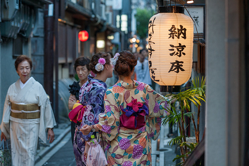 Different generations of women wearing Kimonos. Two old ladys walking and two young ladys taking a selfie on the Street at Kiyamachi-dori, Kyoto, Japan