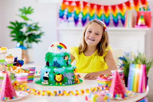 Kids birthday party. Child blowing candles on cake and opening presents on jungle theme celebration. Sweets and cakes for children event. Kid celebrating birthday. Table setting with gifts and pastry.