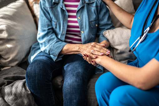 Close-up of a senior woman and nurse holding hands