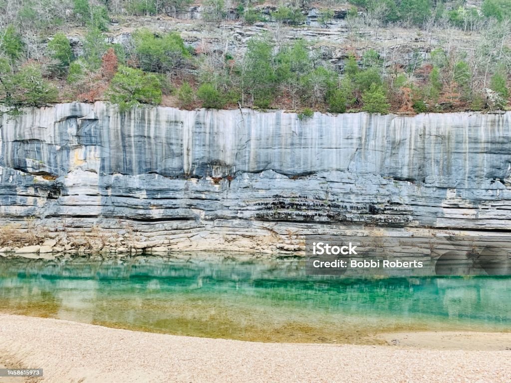Riverside Rock Cliff Teal colored river beneath a gray silver rock face Backgrounds Stock Photo