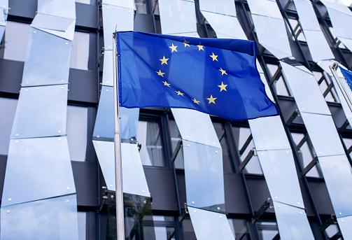 EU flag on the background of a glass office building with a geometric unusual design. The symbol of European countries united in one union